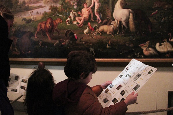 Kids looking at their list of must find items in front of a painting at the vatican