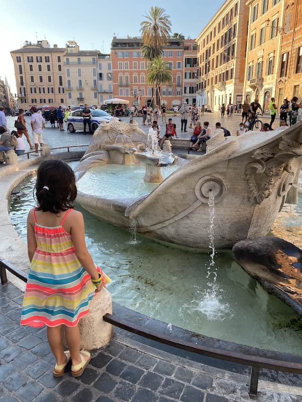 Little girl in rainbow dress standing beside fountain in Piazza di Spagna in Rome, Italy 