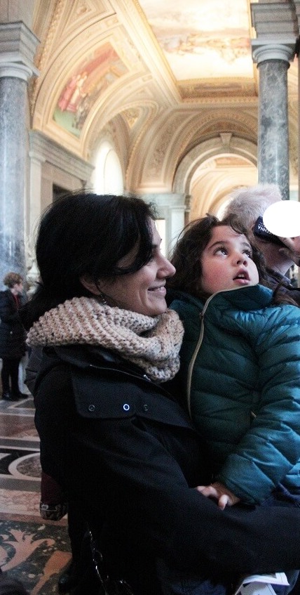 Our family visiting the Vatican with kids: me holding my daughter in one of the Vatican Museum galleries, with her looking at art