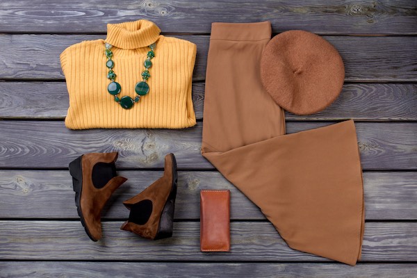 Flat lay of winter clothes including a warm yellow sweater and large green necklace