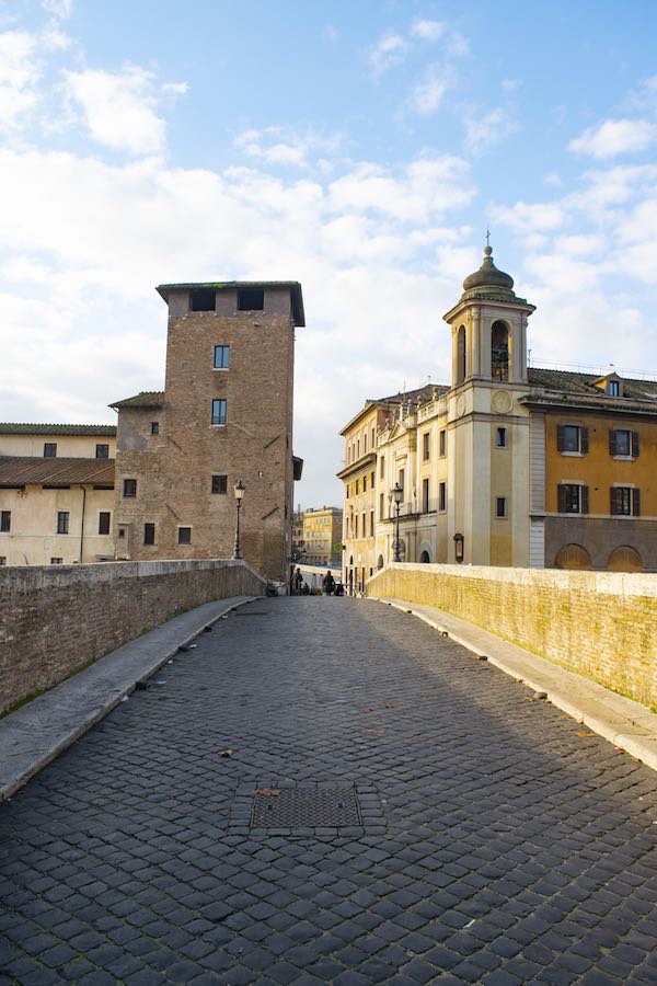 Bridge leading onto Tiber Island with cobbles and medieval tower in the background