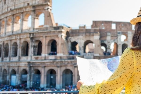 Tourist woman in yellow top looking at map in front of Rome Colosseum