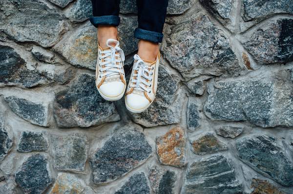 Close up of cream walking shoes worn by a woman sitting on a very wall