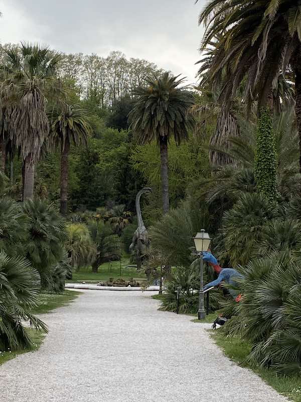 Main path in Rome botanical gardens with tall palm trees and dinosaur sculpture