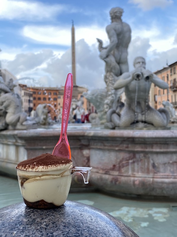 Cup of take out tiramisu against the backdrop of Rome Piazza Navona